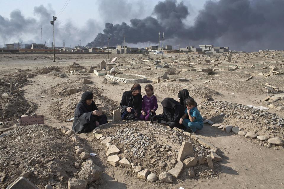 FILE - A family grieves over the grave of a family member at a graveyard damaged by Islamic State extremists in Qayara, some 31 miles, 50 km, south of Mosul, Iraq, Thursday, Oct. 27, 2016. When IS overran Qayara more than two years ago, the extremist group began destroying headstones at the local graveyard, telling residents they were forbidden because they did not exist at the time of the prophet. (AP Photo/Marko Drobnjakovic)