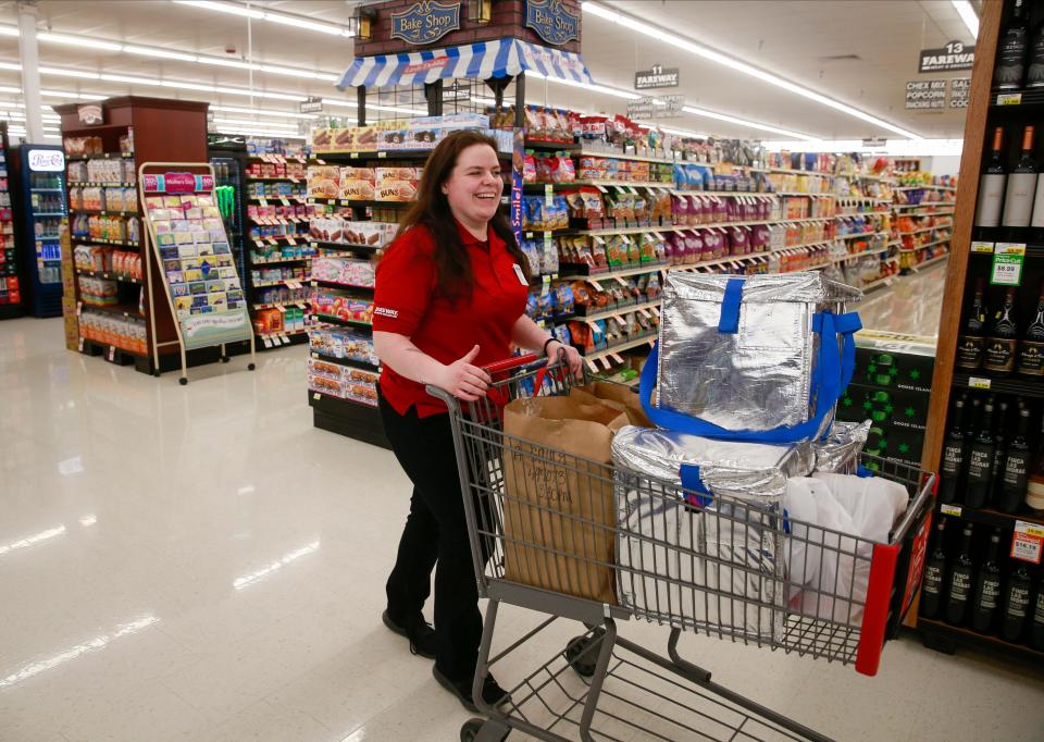 Elana Busick, an employee at Fareway in Des Moines, takes a cart of groceries outside to a customer who placed an online order. The current Fareway uniform is a contrast of red and black.