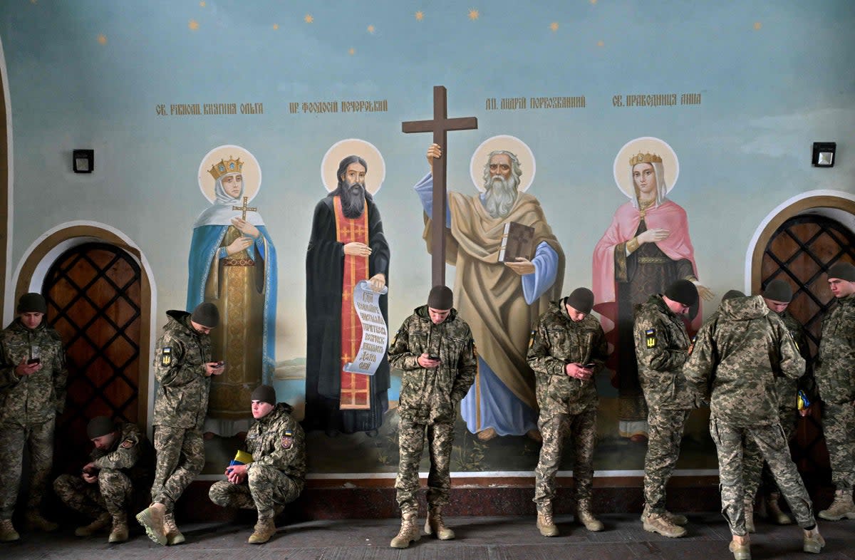 Ukrainian servicemen look at their phones as they shelter from the rain in St Michael’s Cathedral in Kyiv  (AFP/Getty)