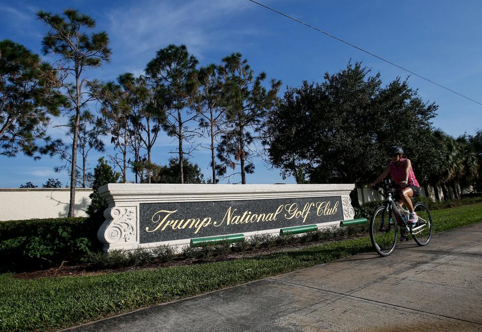 A bicyclist rides by the sign of Trump National Golf Club in Jupiter. The Palm Beach County Property Appraiser's office has estimated that the  club's golf course and buildings could generate as much as $381,328 in taxes for 2023.