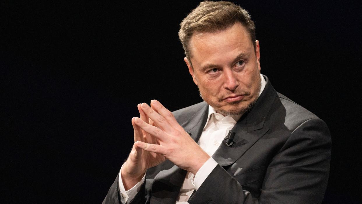  Elon Musk steepling his hands and looking sombre. 