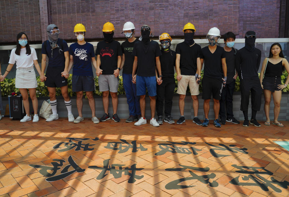 Students from Hong Kong University join their hands and shout slogans near Chinese calligraphy on the floor outside their school in Hong Kong, Monday, Sept. 9, 2019. Thousands of students formed human chains outside schools across Hong Kong on Monday to show solidarity after violent weekend clashes to push for democratic reforms in the semiautonomous Chinese territory. The calligraphy reads "Free Hong Kong, Revolution of Our Times." (AP Photo/Vincent Yu)