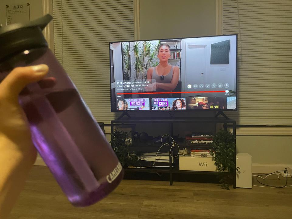 Me holding my water bottle as a Pilates Body Raven video plays on the TV.
