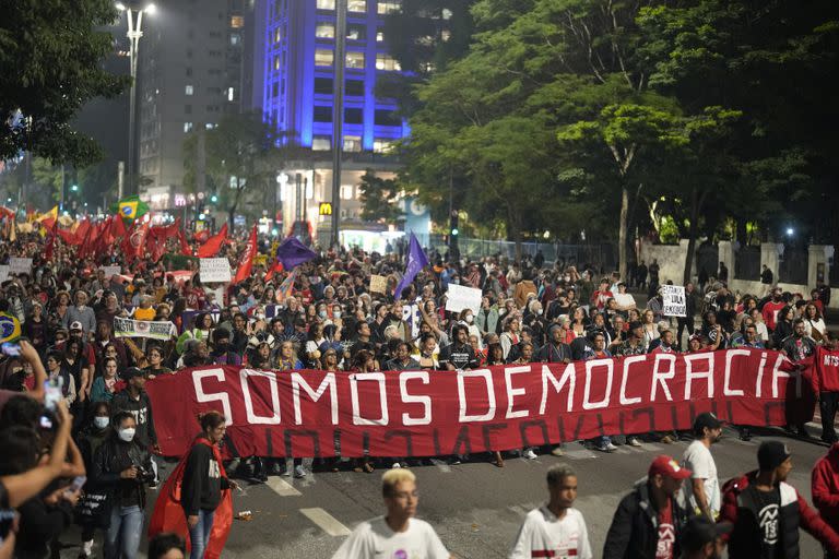 Manifestantes marchan con una bandera que dice "Somos democracia" durante una protesta para reclamar la protección de la democracia del país, en Sao Paulo, Brasil, el lunes 9 de enero de 2023. (AP Foto/Andre Penner)