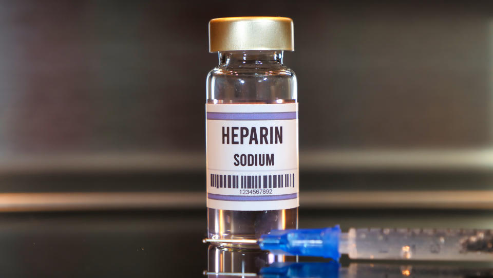 Heparin drug and syringe on black table with reflections and stainless background.