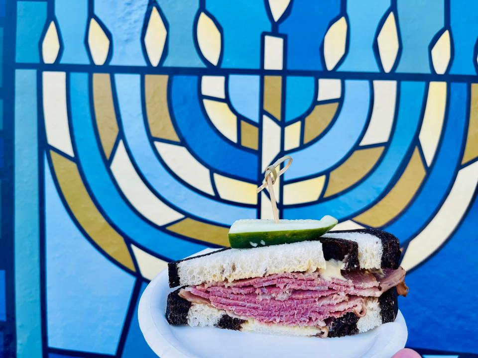 hand holding up a pastrami sandwich in front of a menorah decoration at disney world