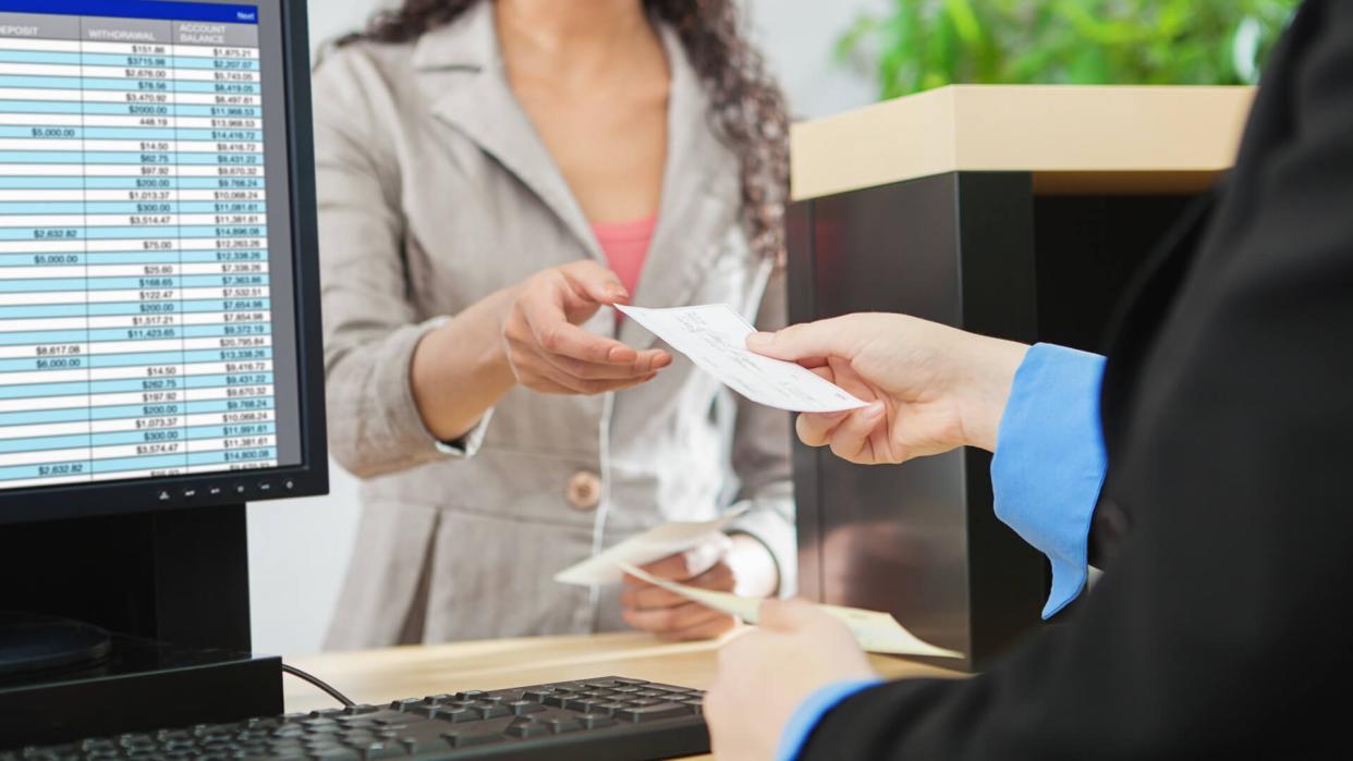 Over-the-shoulder shot of a transaction between a bank teller and a customer in a retail bank.