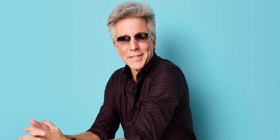 man in sunglasses sitting against a blue background