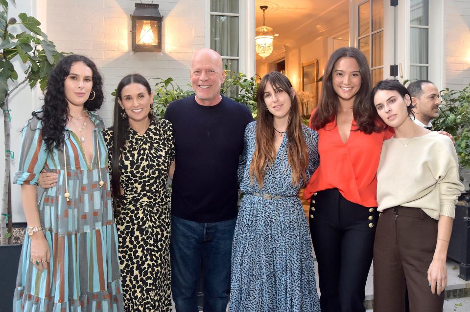 Rumer Willis, Demi Moore, Bruce Willis, Scout Willis, Emma Heming Willis, and Tallulah Willis posing together outside a white building with an open doorway and a lit lantern.