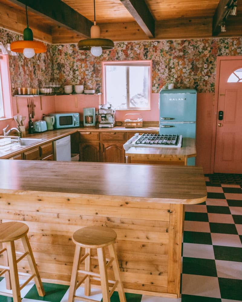Green and white checkerboard floors in pink kitchen with floral wallpaper.