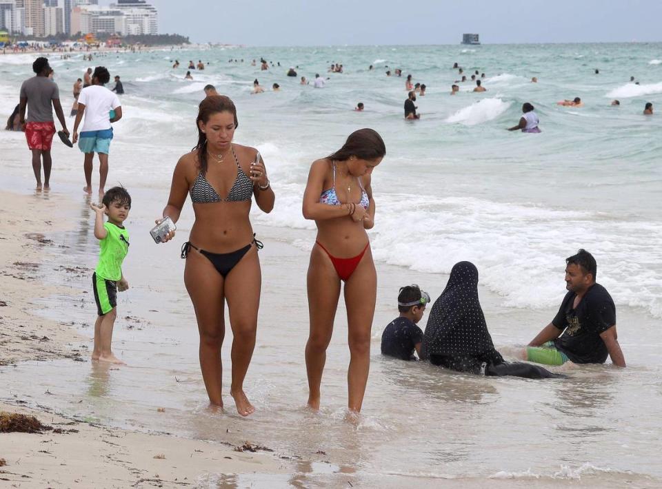 Zain Shoaib, 3, left, plays in the surf, as two young women pass by his family — brother Saaem Shoaib, 5, mother Isbah Sulaiman and father Mohammed Shoaib, right, at South Beach on Labor Day, Sept. 7, 2020. Many tourists, who came for the holiday weekend due to cheap flights and hotels, were not aware that Miami-Dade County had imposed a 10 p.m. curfew due to COVID-19.