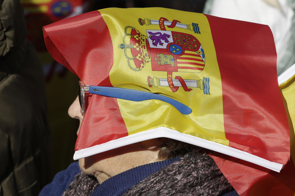 A woman with a Spanish flag covering her head listens to speeches in a rally to promote 'Spanish Unity' during a rally by the right wing VOX party in Madrid, Spain, Saturday, Oct. 26, 2019. The VOX rally comes 2 days after the exhumation and reburial of Spanish dictator Gen. Francisco Franco from the grandiose Valley of the Fallen mausoleum outside Madrid to their new resting place at the Mingorrubio cemetery, 57 kilometers (35 miles) away. (AP Photo/Paul White)