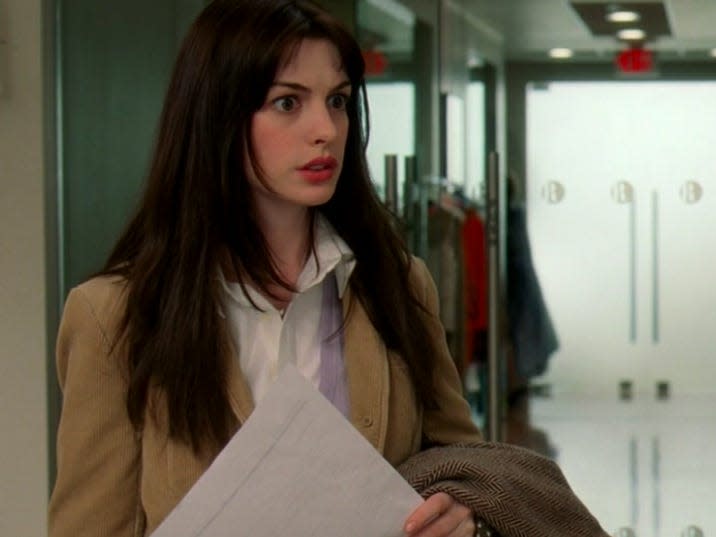 Anne Hathaway as Andy in Devil Wears Prada looking disheveled and holding a pice of paper