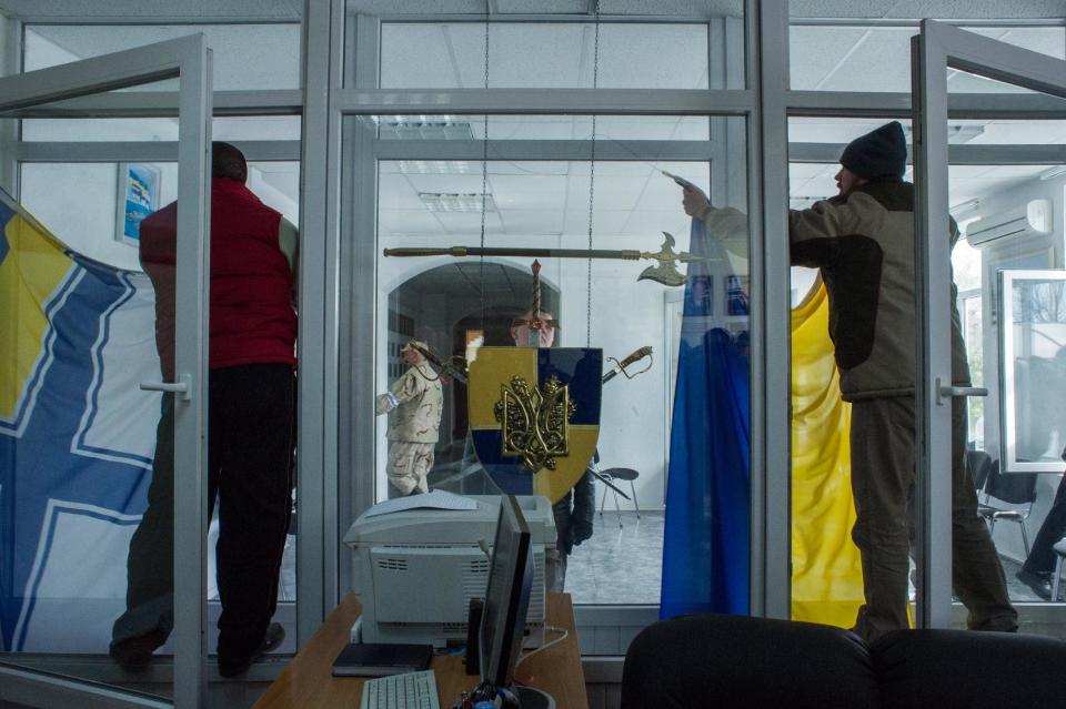 Members of a Pro-Russian self-defense force remove a Ukrainian Navy flag, left, as the other removes the Ukrainian flag at the Ukrainian Navy headquarters in Sevastopol, Crimea, Wednesday, March 19, 2014. An Associated Press photographer said several hundred militiamen took down the gate and made their way onto the base. They then raised the Russian flag in the square by the headquarters. The unarmed militia waited for an hour on the square before the move to storm the headquarters. Following the arrival of the commander of the Russian Black Sea fleet, the Crimeans took over the building. (AP Photo/Andrew Lubimov)