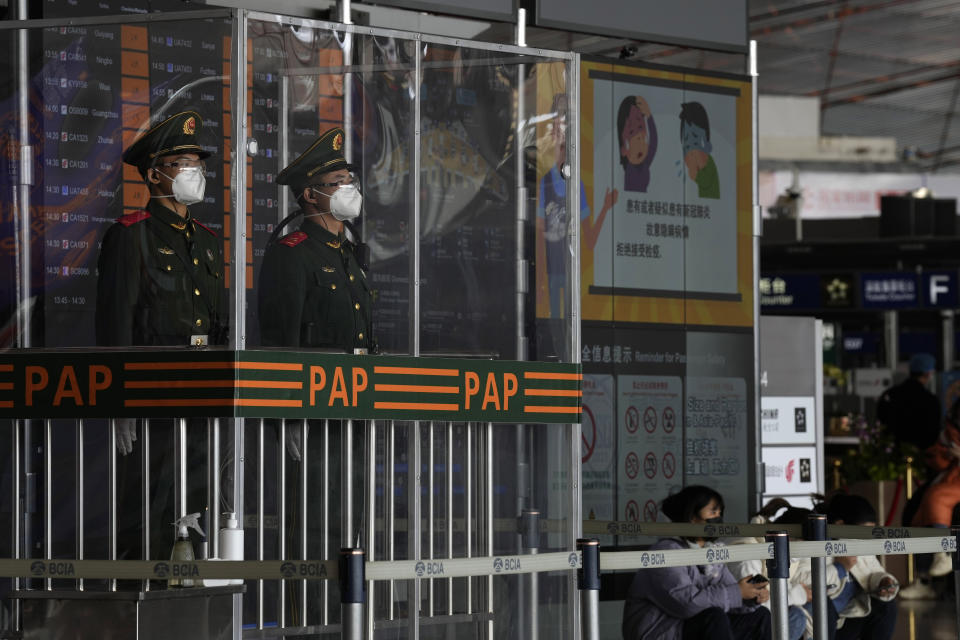 Chinese paramilitary police officers wearing masks stand guard at their post near a display warning against hiding COVID-19 symptoms at the Capital airport terminal in Beijing, Tuesday, Dec. 13, 2022. Some Chinese universities say they will allow students to finish the semester from home in hopes of reducing the potential of a bigger COVID-19 outbreak during the January Lunar New Year travel rush. (AP Photo/Ng Han Guan)