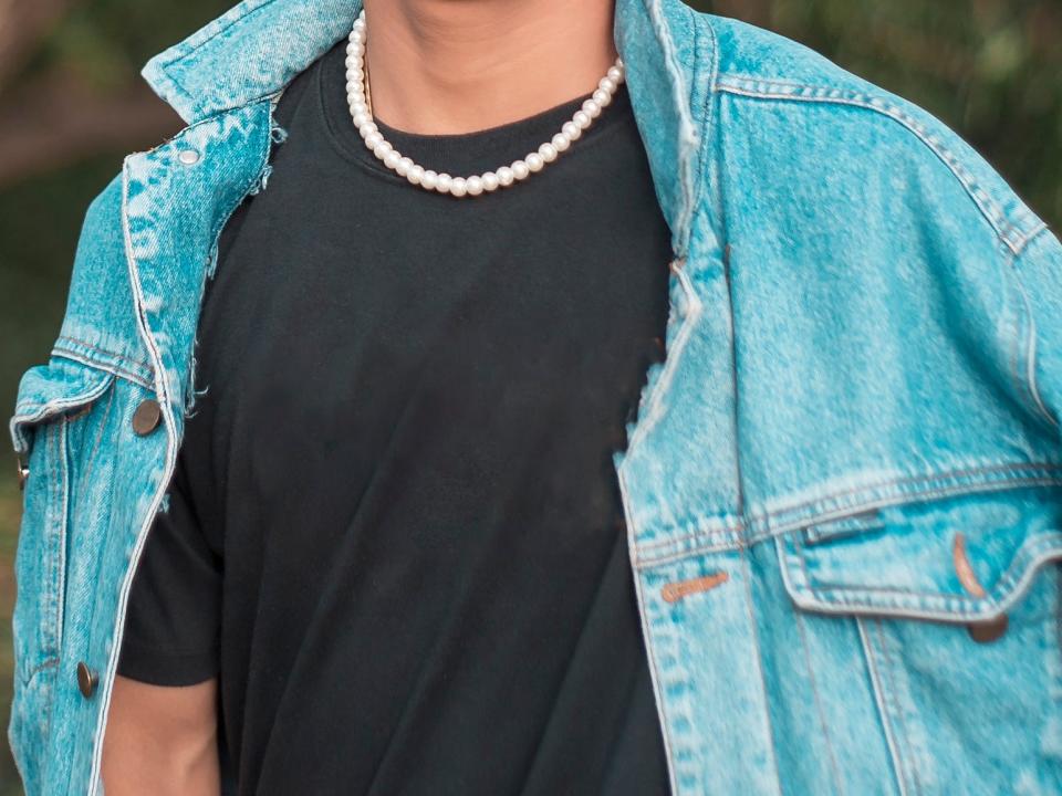 man wearing a jean jacket, black t shirt, and pearl necklace