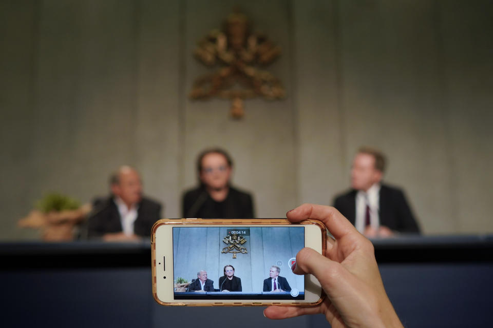 A woman records with a smartphone as U2 rock band frontman Bono Vox talks to reporters during a press conference he held at the end of a meeting with Pope Francis, at the Vatican, Wednesday, Sept. 19, 2018. (AP Photo/Andrew Medichini)