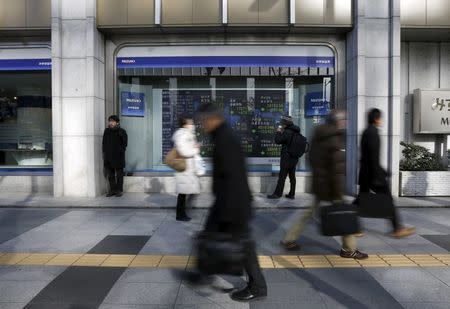 A pedestrian looks an electronic board showing the stock market indices of various countries outside a brokerage in Tokyo, Japan, February 3, 2016. REUTERS/Yuya Shino