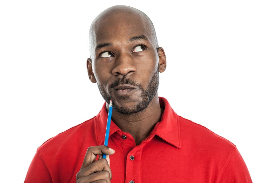 A young black man holds a pencil up to his mouth trying to decide something.