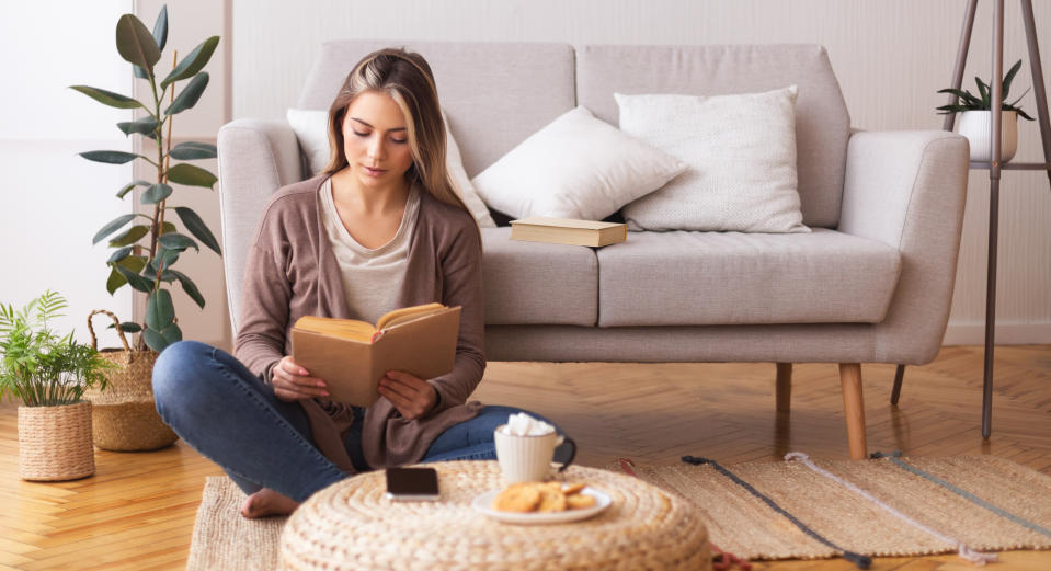 Self education concept. Young woman reading book, sitting on floor at home, panorama, free space