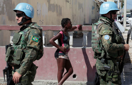 A woman stands next to two Brazilian peacekeepers as they secure the perimeter of the Lycee Philippe Guerrier before the visit of UN Secretary General Ban Ki Moon after Hurricane Matthew in Les Cayes, Haiti, October 15, 2016. REUTERS/Andres Martinez Casares
