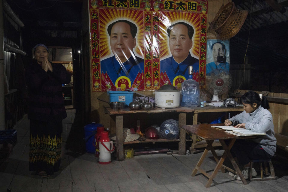 Villagers go about their evening near posters depicting Mao Zedong in Manhaguo village in southern China's Yunnan province on Wednesday, Dec. 2, 2020. Residents said a nearby cave had been used as a sacred altar presided over by a Buddhist monk _ precisely the kind of contact between bats and people that alarms scientists. (AP Photo/Ng Han Guan)