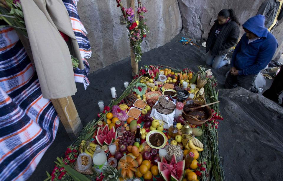 FILE - Locals pray by an offering of food as they hold a ceremony on the slopes of the Popocatepetl volcano in Mexico, March 12, 2014. People from the villages surrounding the volcano trek up its slopes to make offerings and play music in asking the mountain to spare them from eruptions. (AP Photo/Eduardo Verdugo, File)