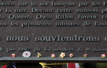 Canadian lapel pins are seen below a plaque which reads in French, "We Will Remember" at the former D-Day landing zone of Juno Beach in Bernieres-sur-Mer, France June 6, 2014. REUTERS/Chris Helgren