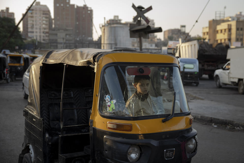 In this Nov. 19, 2019 photo, a boy sits in the driver's seat of a tuk-tuk at a slum in Cairo, Egypt. Motorized rickshaws known as tuk-tuks have ruled the streets of Cairo’s slums for the past two decades hauling millions of Egyptians home every day. Now the government is taking its most ambitious stand yet against the polluting three-wheeled vehicles: to modernize the neglected transport system, it plans to replace tuk-tuks with clean-running minivans. (AP Photo/Nariman El-Mofty)