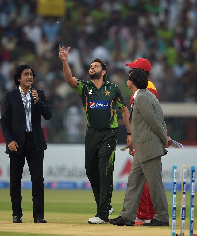 Pakistan's captain Shahid Afridi (C) tosses a coin as he stands next to his Zimbabwe counterpart Elton Chigumbura (red cap) before the start of the first International T20 match at the Gaddafi Cricket Stadium in Lahore