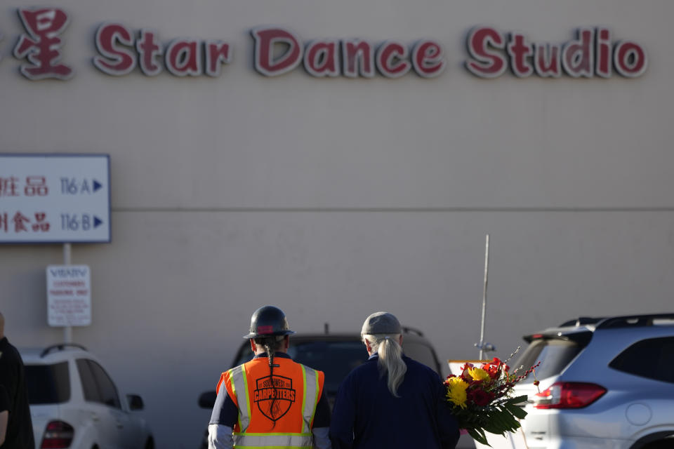 Two men walk to the Star Ballroom Dance Studio holding flowers on Monday, Jan. 23, 2023, in Monterey Park, Calif. A gunman killed multiple people at the ballroom dance studio late Saturday amid Lunar New Year's celebrations in the predominantly Asian American community. (AP Photo/Ashley Landis)