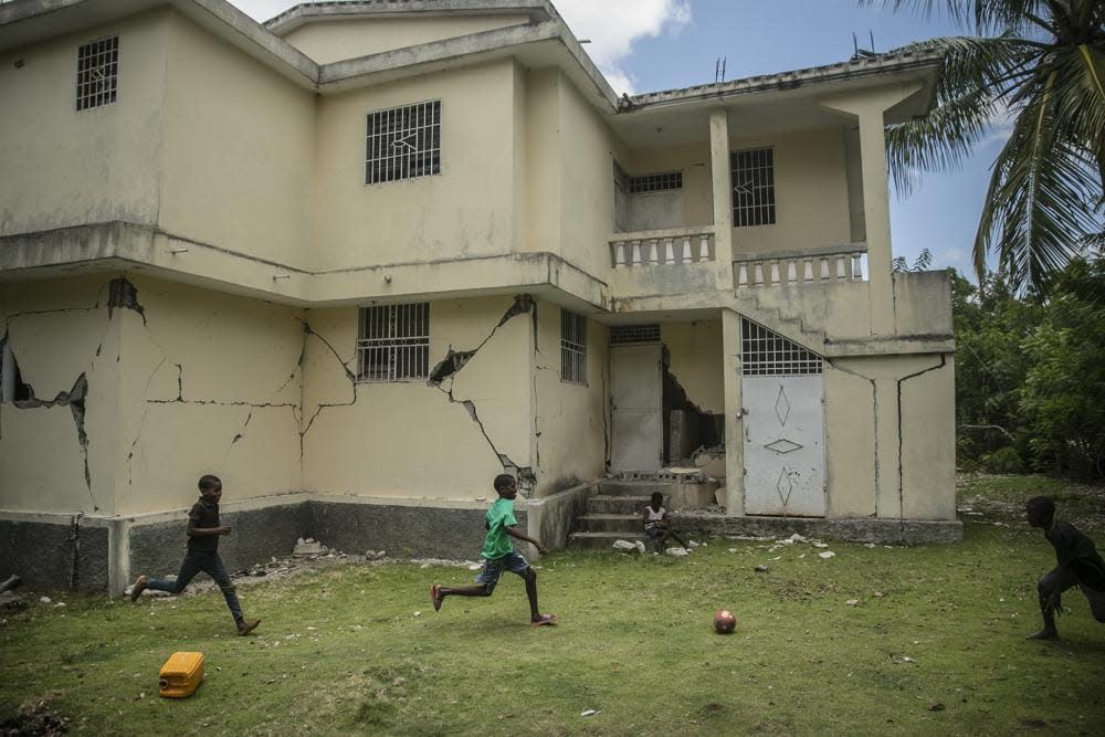 Children play football next to a house damaged a year ago by a magnitude-7.2 earthquake, in Maniche, Haiti, Thursday, Aug. 18, 2022. (AP Photo/Odelyn Joseph)