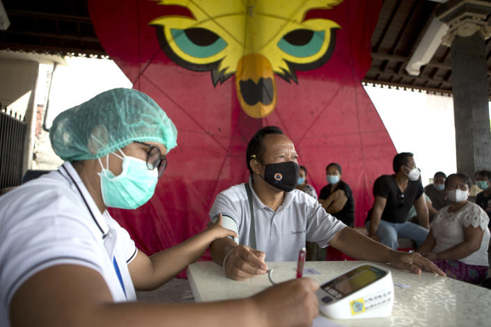 A health worker checks vital signs of an elderly man before a booster shot of Moderna COVID-19 vaccine during a third dose vaccination campaign in Denpasar, Bali, Indonesia Saturday, Jan. 29, 2022. (AP Photo/Firdia Lisnawati)