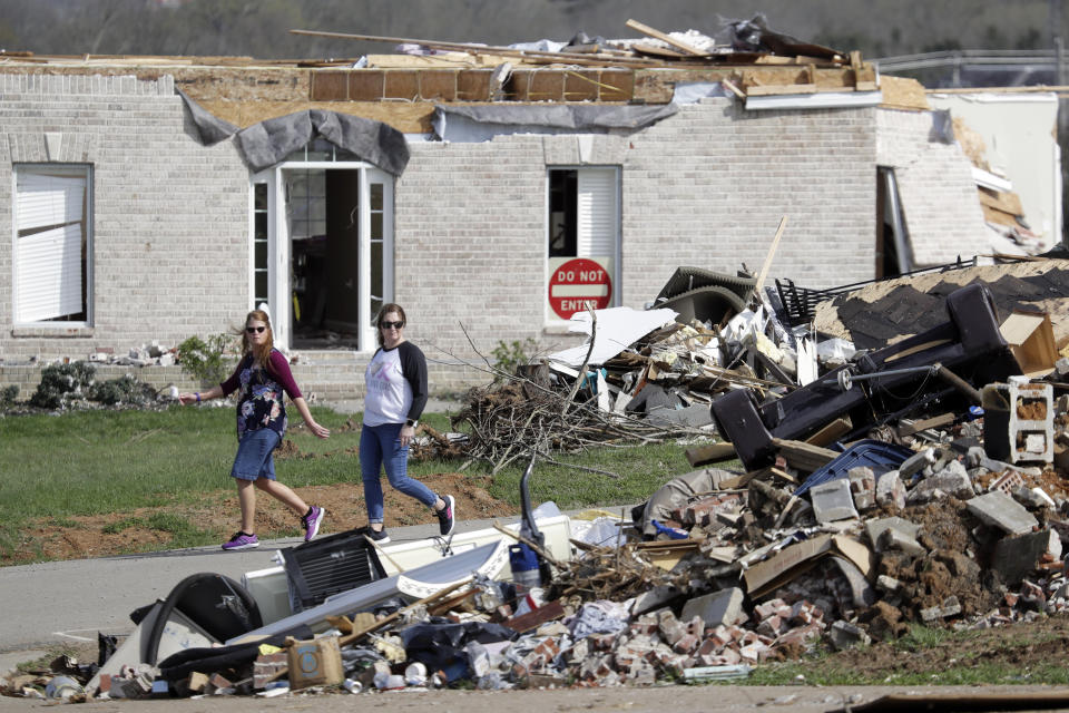 In this March 26, 2020, photo, people walk down a street lined with tornado debris in Gallatin, Tenn. Thousands of people in Middle Tennessee affected by the deadly twisters of March 3 now also have to confront life in the age of coronavirus. (AP Photo/Mark Humphrey)