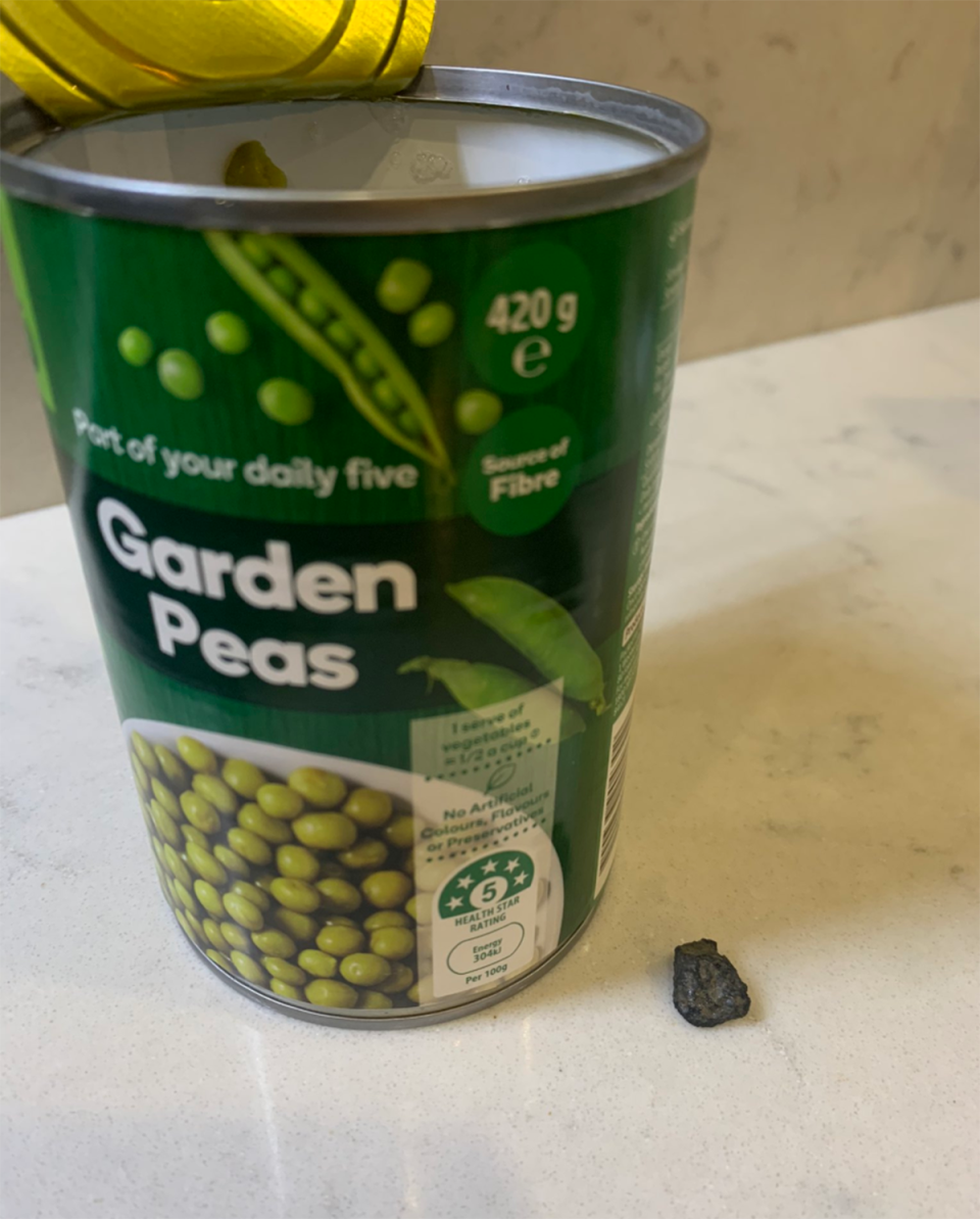 Can of Woolworths brand garden peas next to a small rock.