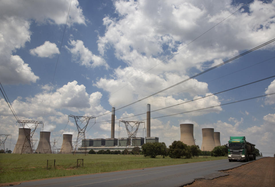 FILE - A coal truck, right, passes the coal-powered Duvha power station, near Emalahleni (formerly Witbank) east of Johannesburg, on Nov. 17, 2022. The electricity shortages that plague many of Africa's 54 countries are a serious drain on the continent's economic growth. In recent years South Africa's power generation has become so inadequate that the continent's most developed economy must cope with rolling power blackouts of eight to 10 hours per day. (AP Photo/Denis Farrell, File)