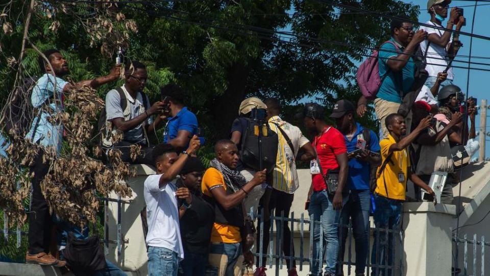 Un grupo de haitianos toma fotos y observa la llegada de policías kenianos