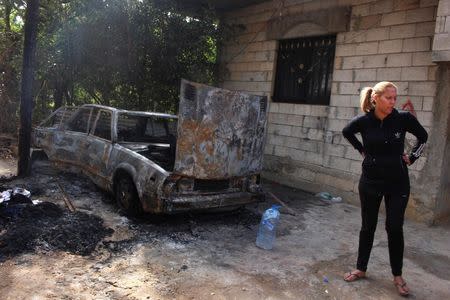 A woman stands near a burnt vehicle in the village of Bihnin, northern Lebanon, following clashes between Lebanese soldiers and Islamist gunmen, October 27, 2014. REUTERS/Stringer