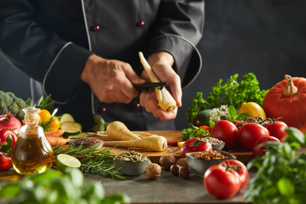 chef peeling carrot over board with veggies in background