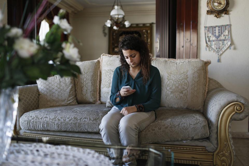 Farah Baker, 16, uses her phone to tweet in her family's home in Gaza City, August 10, 2014. As bombs explode in Gaza, Palestinian teenager Farah Baker grabs her smartphone or laptop before ducking for cover to tap out tweets that capture the drama of the tumult and fear around her. The 16-year-old's prolific posts on Twitter have made her a social media sensation through the month-old conflict. Once a little known high school athlete, Baker's following on the Web site has jumped from a mere 800 to a whopping 166,000. Picture taken August 10, 2014. REUTERS/Siegfried Modola (GAZA - Tags: MEDIA SCIENCE TECHNOLOGY POLITICS CIVIL UNREST CONFLICT)