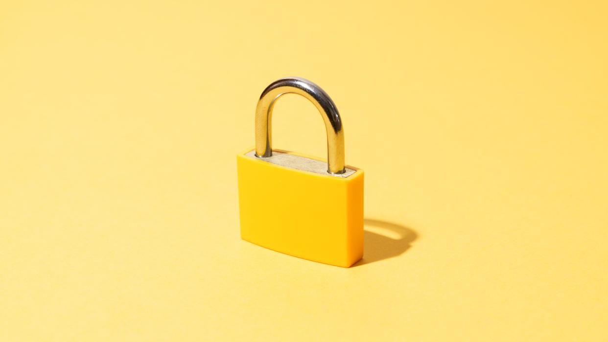  A yellow padlock standing centrally in front of a flat pale yellow background 