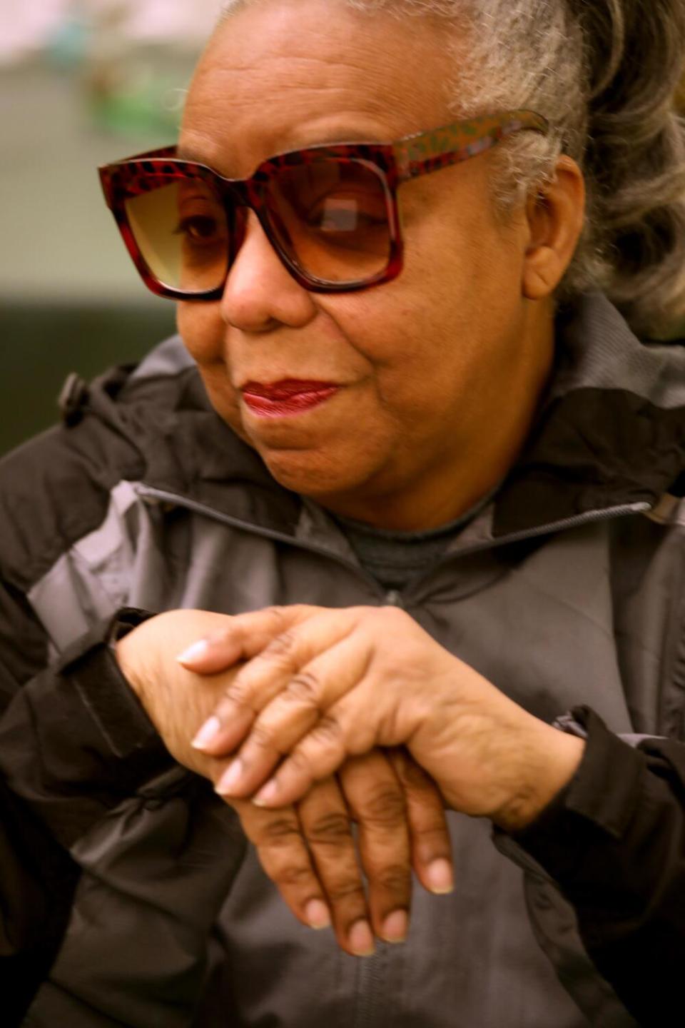 A woman in large sunglasses sits with her hands clasped in front of her