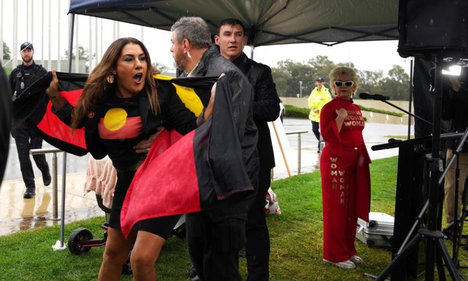 Senator Lidia Thorpe with an Aboriginal flag draped around her shoulders being blocked from accessing the lectern where Kellie-Jay Keen can be seen standing.