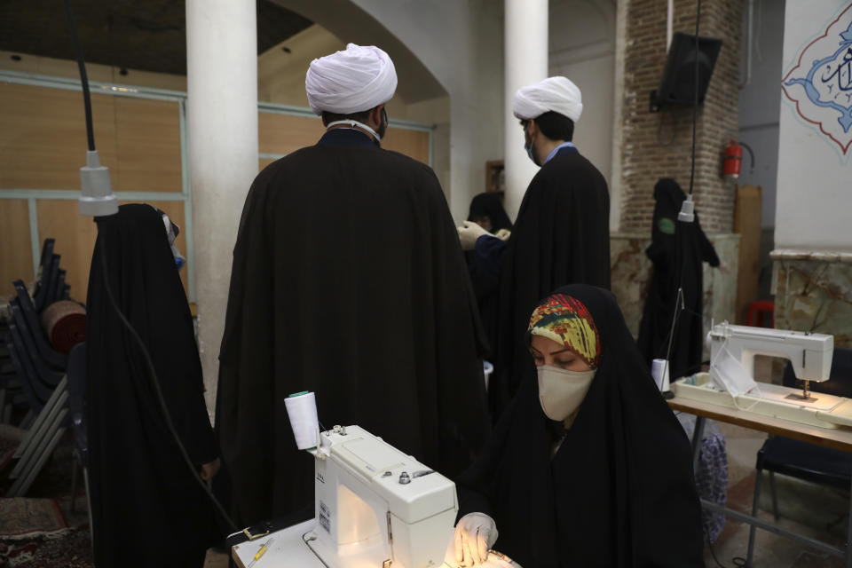 Two clerics visit a workshop where volunteer woman sew bed sheets for hospitals, in a mosque in southern Tehran, Iran, Sunday, April 5, 2020. Iran is battling the worst new coronavirus outbreak in the Mideast. (AP Photo/Vahid Salemi)