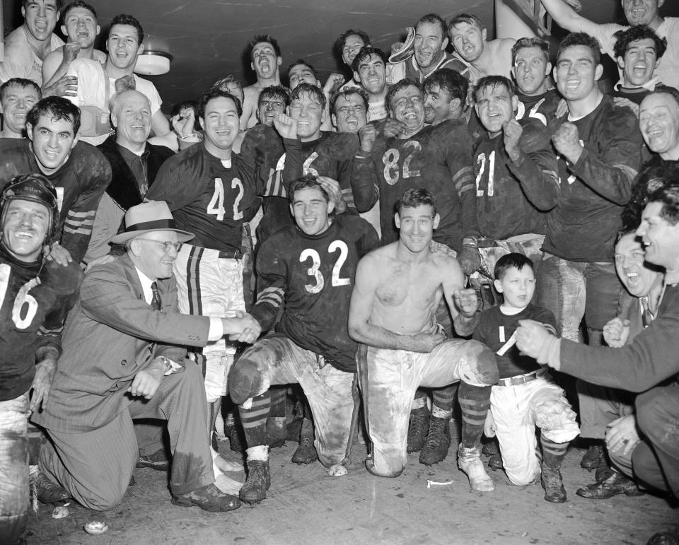 FILE - Chicago Bears' quarterback Johnny Lujack (32) is congratulated by coach George Halas, left, on setting a National League aerial gain record of 468 yards in defeating their rivals, the Chicago Cardinals, in Chicago, Dec. 11, 1949. Other players whooping it up in the dressing room are: Sid Luckman (42), Clyde "Bulldog" Turner (66), behind Lujack, Ray Bray (82), who is being kissed by Don Kindt; George McAfee, shirtless, and Chuck Drulis (21). The rest are unidentified. Lujack, the Heisman Trophy winner who led Notre Dame to three national championships in the 1940s, died in Florida on Tuesday, July 25, 2023, following a brief illness. He was 98.(AP Photo/Ed Maloney, File)