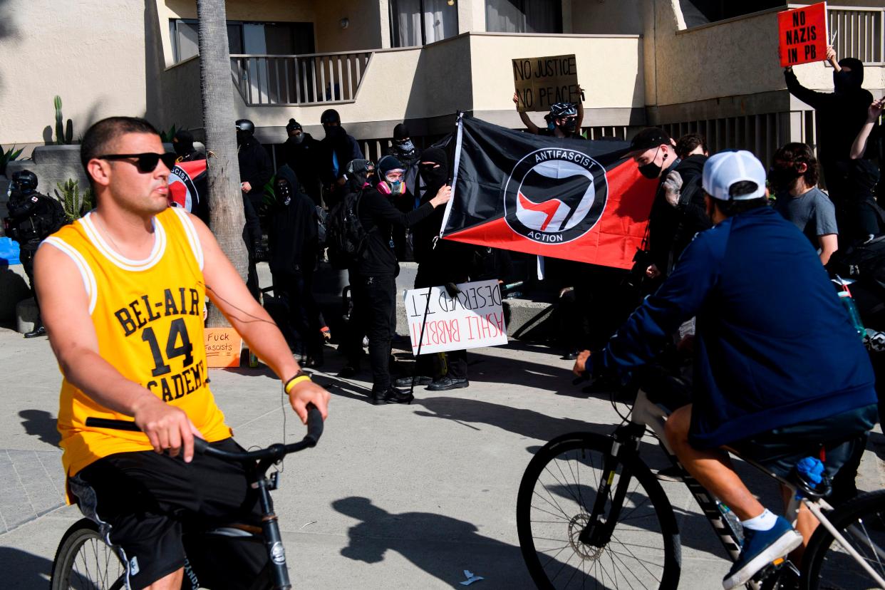People bicycle past counter-protesters, some holding Antifa flags, awaiting demonstrators for a "Patriot March" demonstration in support of US President Donald Trump on Jan. 9, 2021 in the Pacific Beach neighborhood of San Diego, California.
