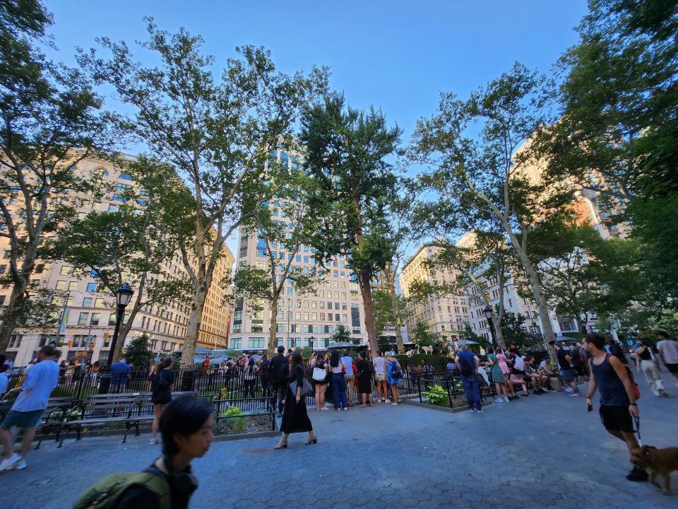 <p>A picture taken with the Galaxy Z Flip 4 showing a wide angle view of many people walking around in a park in New York City, some are gathered around an enclosed dog run.</p>
