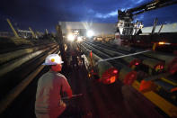 A worker straps down utility poles that were just loaded on their truck before they head out to restore power at dawn, at a tent city for electrical workers in Amelia, La., Friday, Sept. 17, 2021. In the wake of hurricanes, one of the most common and comforting sites is the thousands of electric workers who flow into a battered region when the winds die down to restore power and a sense of normalcy. (AP Photo/Gerald Herbert)