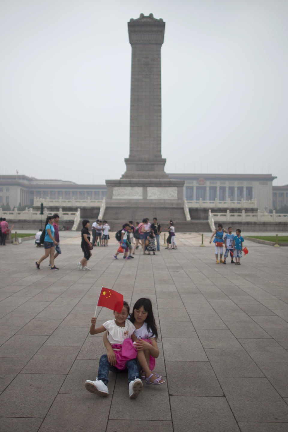 In this Monday, July 9, 2012 photo, a girl waves Chinese national flag while resting with her mom in front of the Monument to People's Heroes on the Tiananmen Square in Beijing, China. Tiananmen Square, the world's largest public square, is surrounded by buildings of political and cultural significance and is visited by thousands of tourists daily. (AP Photo/Alexander F. Yuan)
