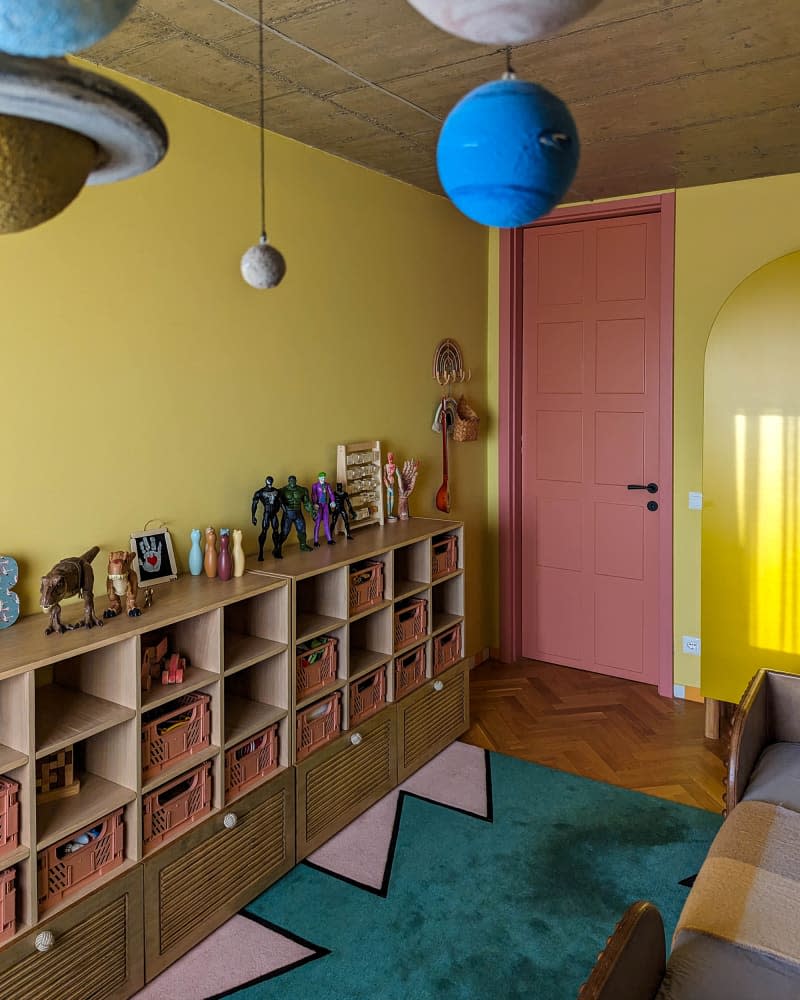 Yellow kids room with solar system mobile and wall of wood cubby shelves